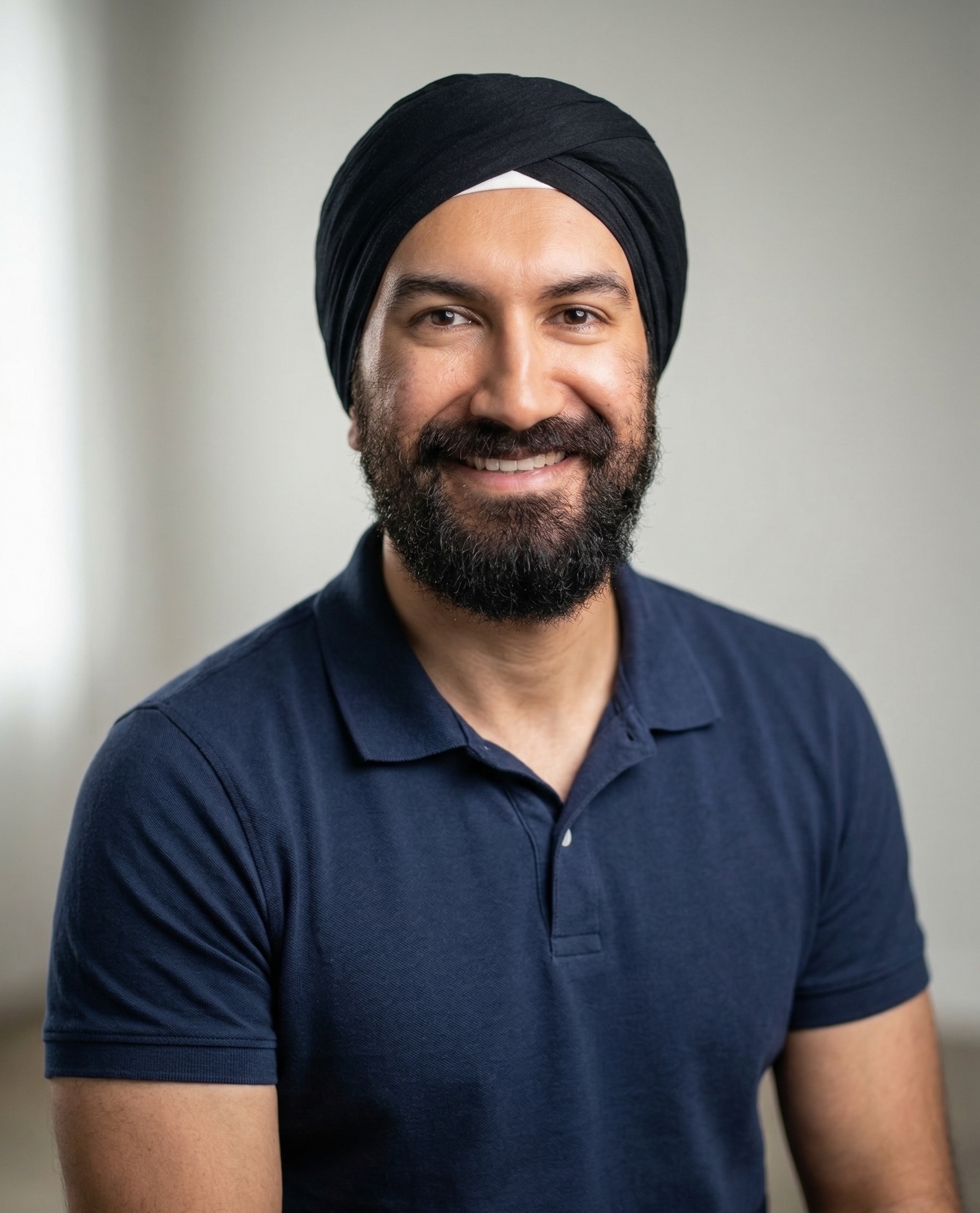 Portrait of Haransh smiling, wearing a black turban and navy polo against a neutral background.